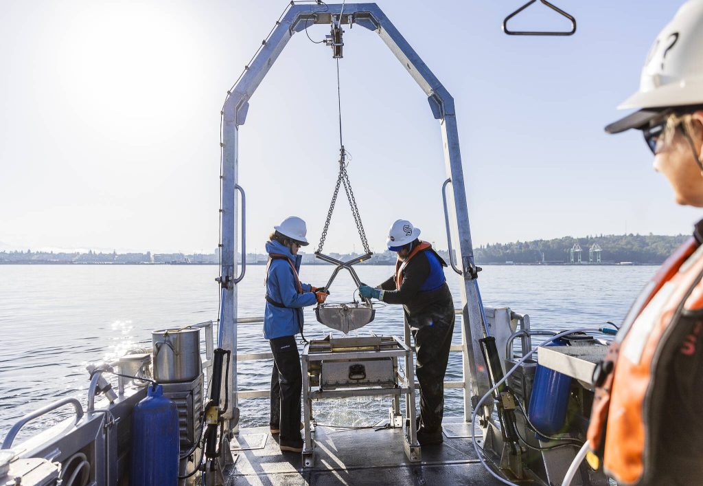 Dany Burgess, left, and Chad Eshelman, right, help maneuver their equipment holding a sediment sample up and onto the boat on Thursday, May 1, 2025 in Everett, Washington. (Olivia Vanni / The Herald)