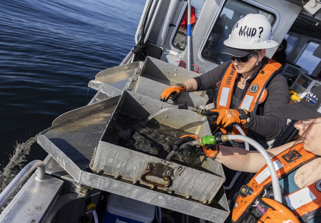 Sandy Weakland, left, and Emma LeValley, right, use water to wash away mud to leave larger pieces of debris and benthic organisms on Thursday, May 1, 2025, in Everett, Washington. (Olivia Vanni / The Herald)