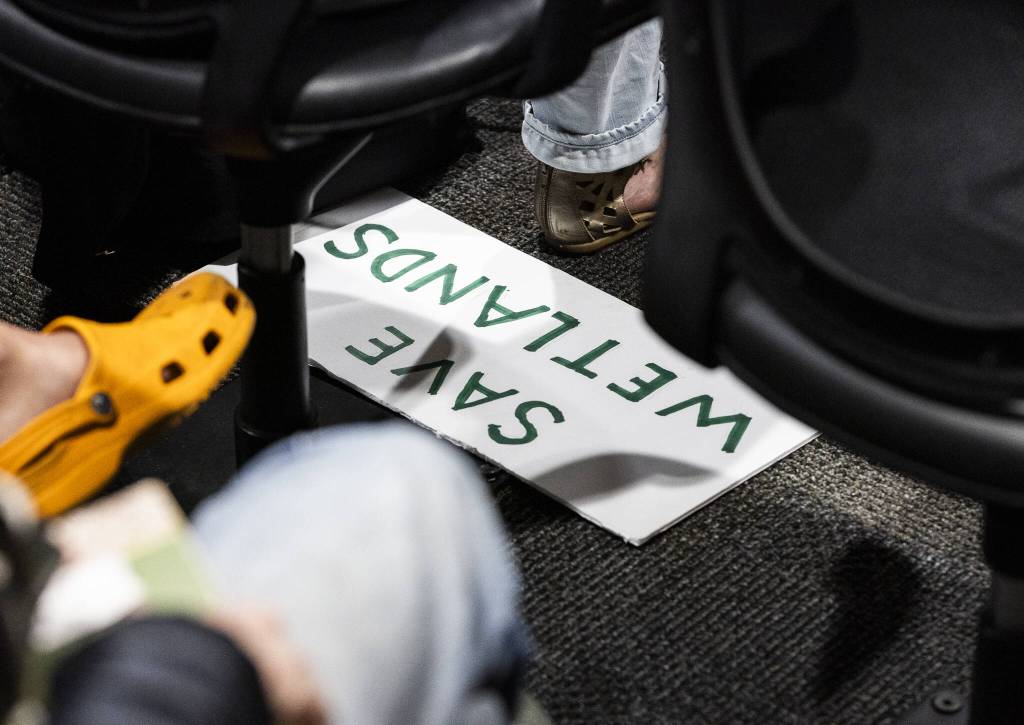 A SAVE WETLANDS poster is visible under an seat during a public hearing about Critical Area Regulations Update on Ordinance 24-097 on Wednesday, May 14, 2025 in Everett, Washington. (Olivia Vanni / The Herald)
