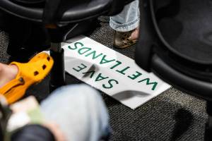 A “SAVE WETLANDS” poster is visible under an seat during a public hearing about Critical Area Regulations Update on ordinance 24-097 on Wednesday, May 14, 2025 in Everett, Washington. (Olivia Vanni / The Herald)