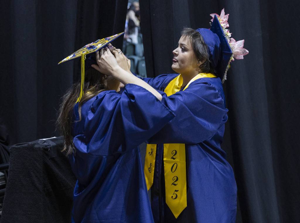 Gabriella Hurley, right, helps secure Anya Kozinas graduation cap before the start of Mariner High Schools 2025 commencement on Friday, June 13, 2025, at Angel of the Winds Arena in Everett, Washington. (Olivia Vanni / The Herald)