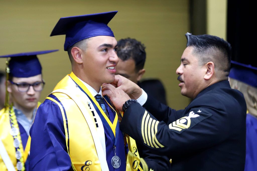 Navy Sr. Chief Joseph Estrella, right, adjusts the gown of graduate  Joshua Tentoea, a member of the Navy Junior Reserve Officers Training Corps  before Everett High School's 2025 commencement on Saturday, June 14, 2025, at Angel of the Winds Arena in Everett, Washington. (Mike Henneke / The Herald)