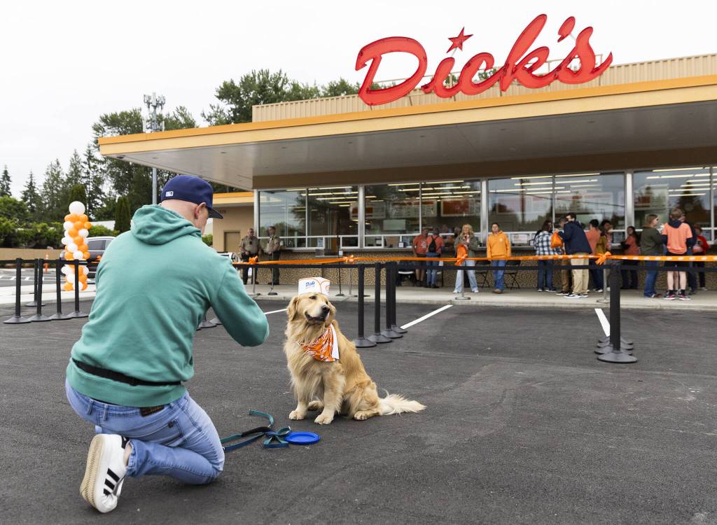 Ande Edlund takes a photograph of his dog Chase wearing a Dicks Drive-In hat before the grand opening on Thursday, June 12, 2025 in Everett, Washington. (Olivia Vanni / The Herald)