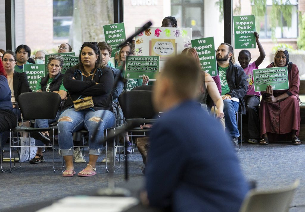 People hold up signs in protest while Everett Community Colleges Vice President of Human Resources Josh Ernst speaks on Thursday, June 26, 2025 in Everett, Washington. (Olivia Vanni / The Herald)