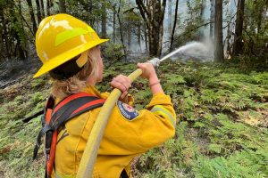A firefighter with Sky Valley Fire sprays water on a hotspot Wednesday, Sept. 14, 2022, along U.S. 2 as the Bolt Creek fire continues to burn between Index and Skykomish. (Peter Mongillo / Snohomish Regional Fire and Rescue)