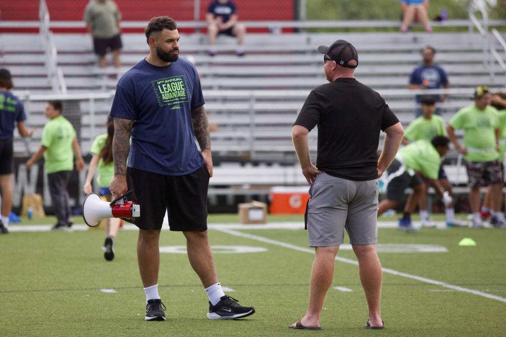 Seattle Seahawks offensive tackle Abraham Lucas (left) talks to Archbishop Murphy football coach Joe Cronin during the third annual League Advantage Youth Football Camp at Lucas alma mater, Archbishop Murphy High School, in Everett, Washington on Saturday, June 28, 2025. (Joe Pohoryles / The Herald)