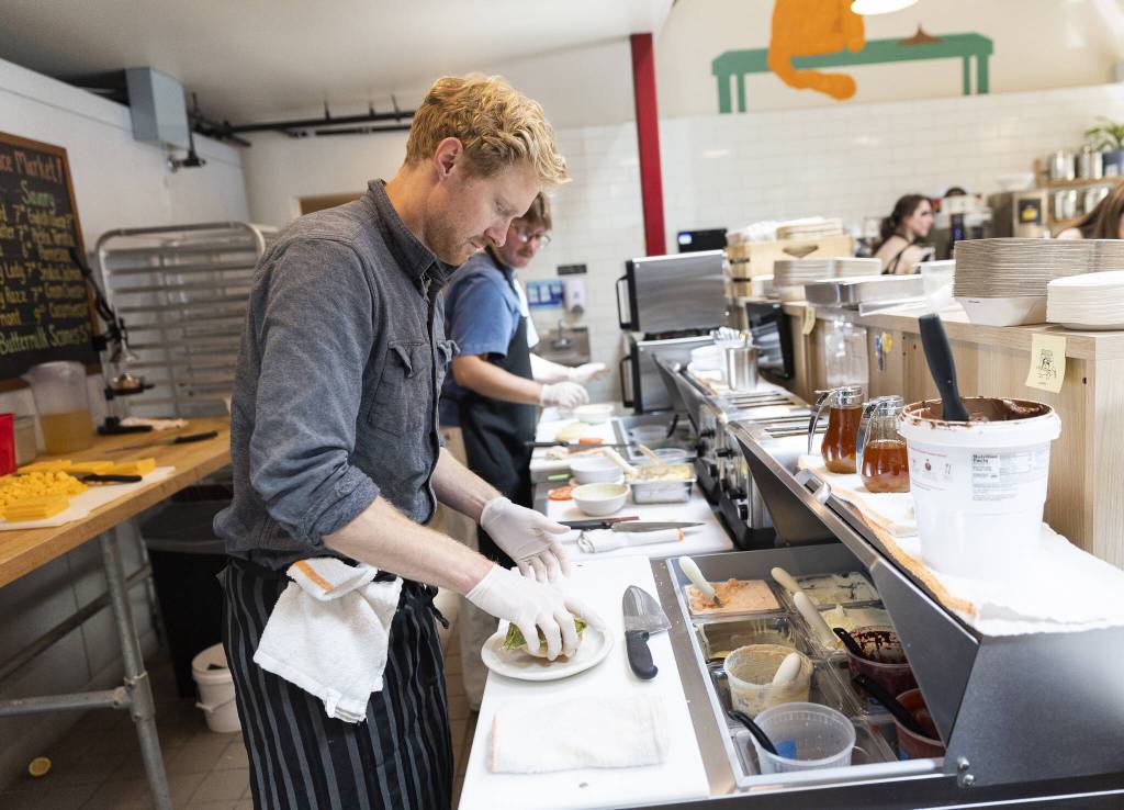 Cooper Golding assembles a Rob’s Favorite crumpet with green egg, English cheese, tomato on smoked salmon cream cheese on Tuesday, June 24, 2025 in Edmonds, Washington. (Olivia Vanni / The Herald)