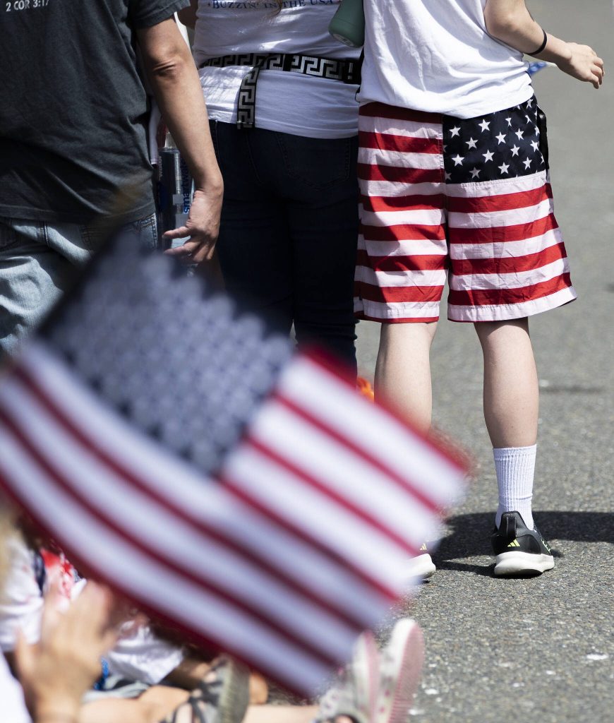 A person wearing American flag shorts watches the Fourth of July parade on Friday, July 4, 2025 in Everett, Washington. (Olivia Vanni / The Herald)