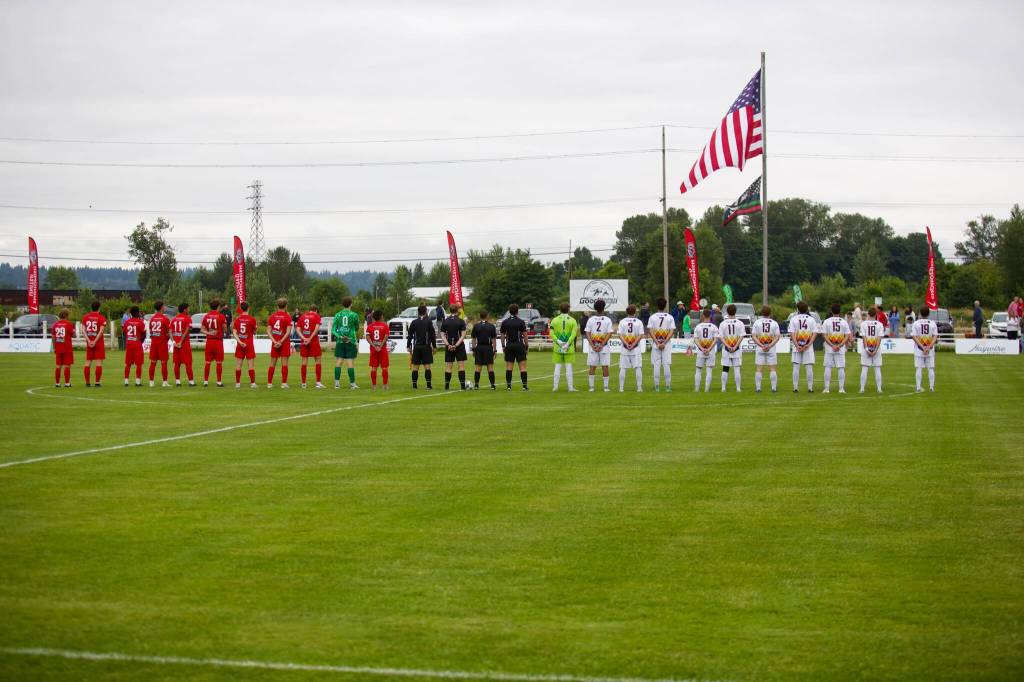 The starting lineups for Snohomish United (left in red) and the Tacoma Stars stand at midfield for the national anthem ahead of Snohomish Uniteds 5-1 win at Stockers Fields on July 9, 2025 (Joe Pohoryles / The Herald)