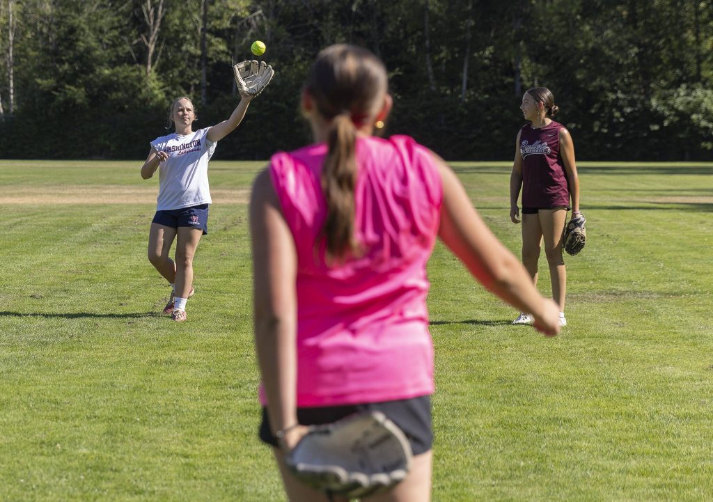 Daphnee Calsyn, 12, left, and Camryn Brown, 12, right play catch with Penelope Gahan, 13, center, for warms up on Wednesday, July 16, 2025 in Mill Creek, Washington. (Olivia Vanni / The Herald)