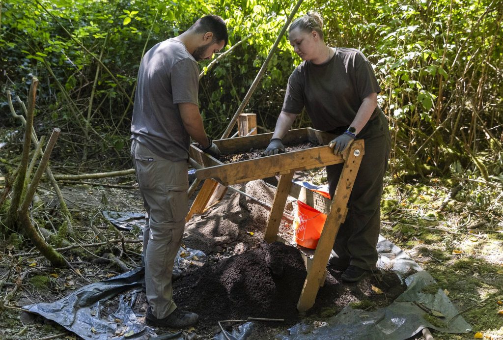 Barrett Massand, left, and Sharon Nettleton, right, sift dirt dug from marked sections of land in Japanese Gulch on Wednesday, July 23, 2025 in Everett, Washington. (Olivia Vanni / The Herald)