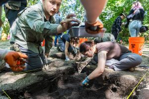 Josh Thiel, left, places a nail into a dust pan while Rey Wall continues digging in a sectioned off piece of land at Japanese Gulch on Wednesday, July 23, 2025 in Everett, Washington. (Olivia Vanni / The Herald)