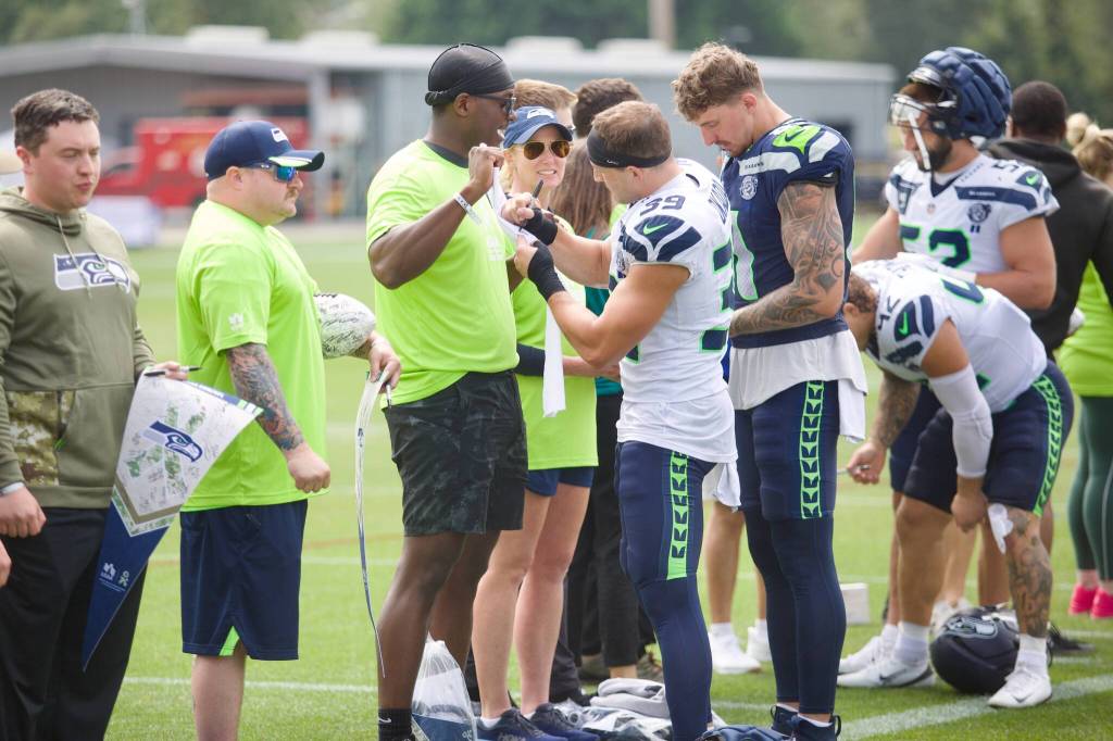 Coast Guard machinery technician Matthew Scriven (center) gets an autograph from Seahawks safety Ty Okada during the USAAs Salute to Service NFL Boot Camp hosted by the Seattle Seahawks at Virginia Mason Athletic Center on Aug. 4, 2025. (Joe Pohoryles / The Herald)