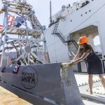Mattie Hanley, wife of DARPA director Stephen Winchell, smashes a bottle to christen the USX-1 Defiant, a first-of-its-kind autonomous naval ship, at Everett Ship Repair on Monday, Aug. 11, 2025 in Everett, Washington. (Olivia Vanni / The Herald)