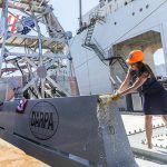 Mattie Hanley, wife of DARPA director Stephen Winchell, smashes a bottle to christen the USX-1 Defiant, first-of-its kind autonomous naval ship, at Everett Ship Repair on Monday, Aug. 11, 2025 in Everett, Washington. (Olivia Vanni / The Herald)