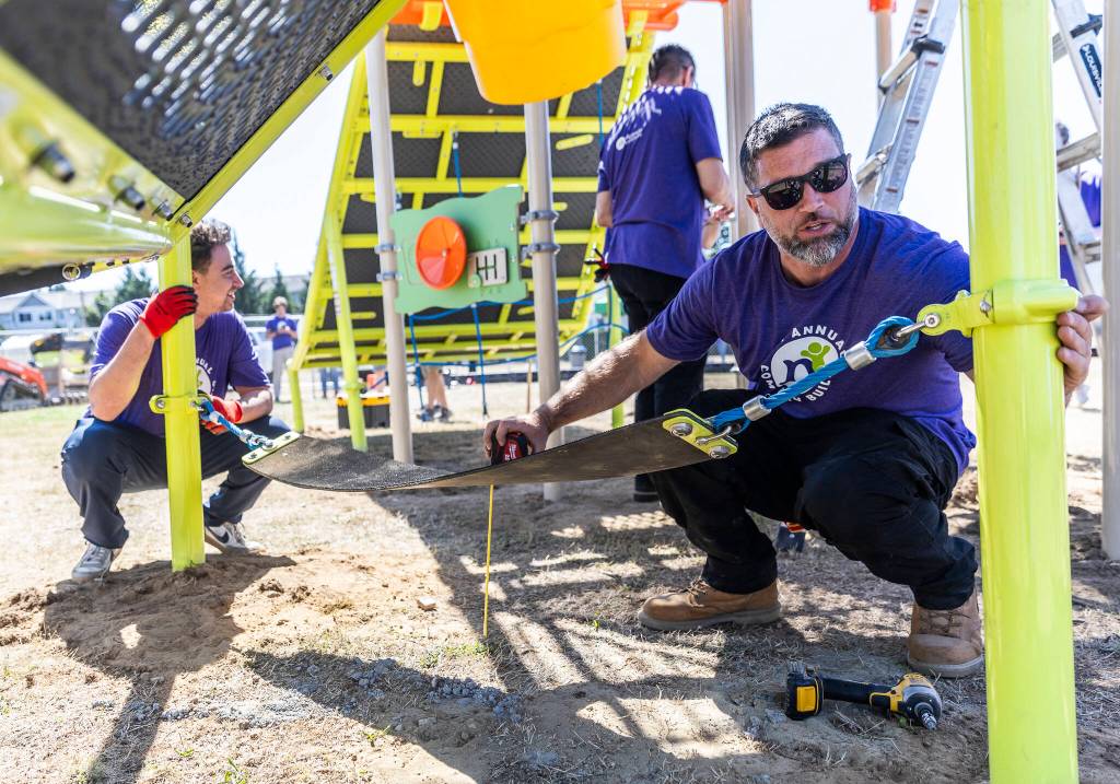 Dustin Deer, right, and Ryan Gordon, left, level a suspended seat on a play structure on Wednesday, Aug. 20, 2025 in Marysville, Washington. (Olivia Vanni / The Herald)