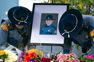 Two troopers place a photo of slain Washington State Patrol trooper Chris Gadd outside district headquarters about 12 hours after Gadd was struck and killed in a crash on southbound I-5 on March 2 in Marysville. (Ryan Berry / The Herald)