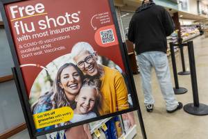 A person waits in line at a pharmacy next to a sign advertising free flu shots with most insurance on Thursday, Feb. 27, 2025 in Everett, Washington. (Olivia Vanni / The Herald)