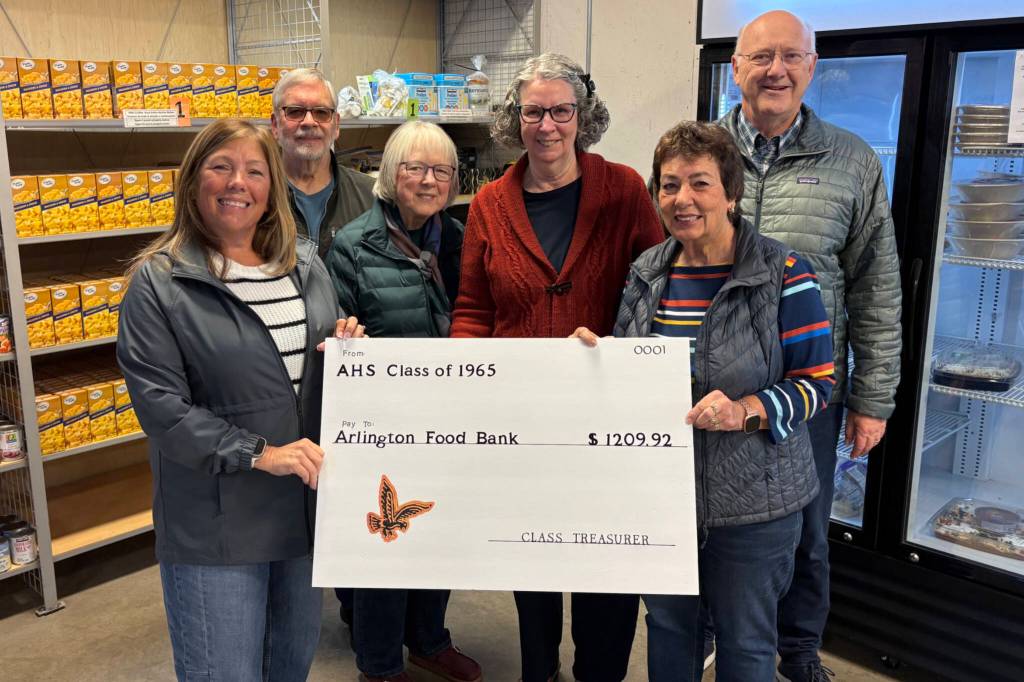 Arlington Community Food Bank Executive Director Carla Rankin, left, stands holding an oversized check with Krista Galde, right, along other members of the Arlington High School class of 1965. Members of the class decided to donate money saved for their next class reunion to the food bank instead. (Taylor Scott Richmond / The Daily Herald)