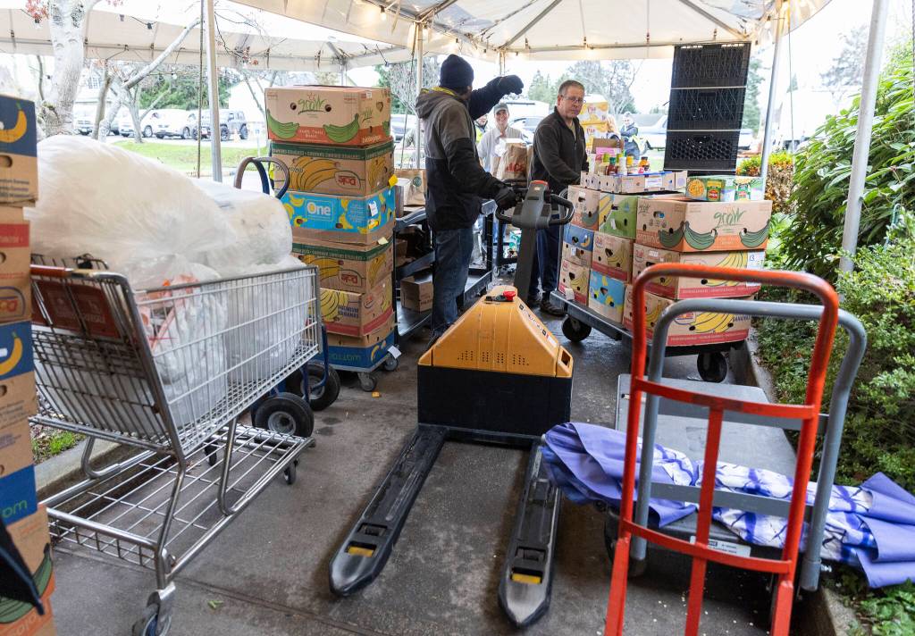 Volunteers and employees navigate through a tented and crowded walkway as donations come in and food is brought out to waiting customers at the Edmonds Food Bank on Dec. 8, 2025, in Edmonds, Washington. (Olivia Vanni / The Herald)