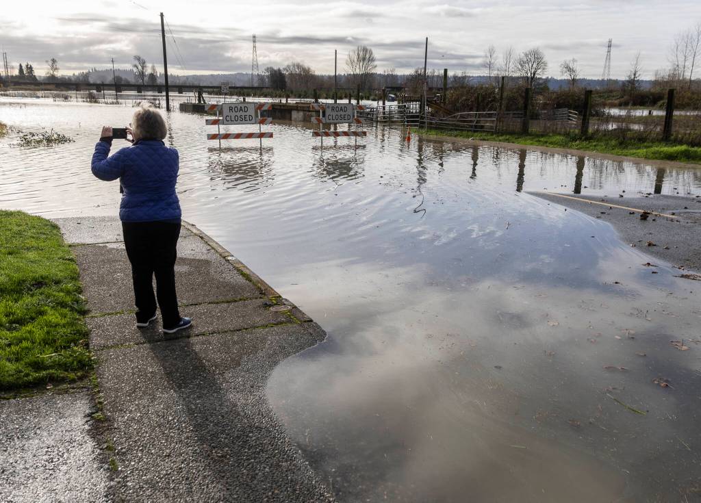 Pam Somers takes a photograph of the floodwater covering Old Snohomish Monroe Road and the Stocker Fields on Tuesday, Dec. 9, 2025 in Snohomish, Washington. (Olivia Vanni / The Herald)