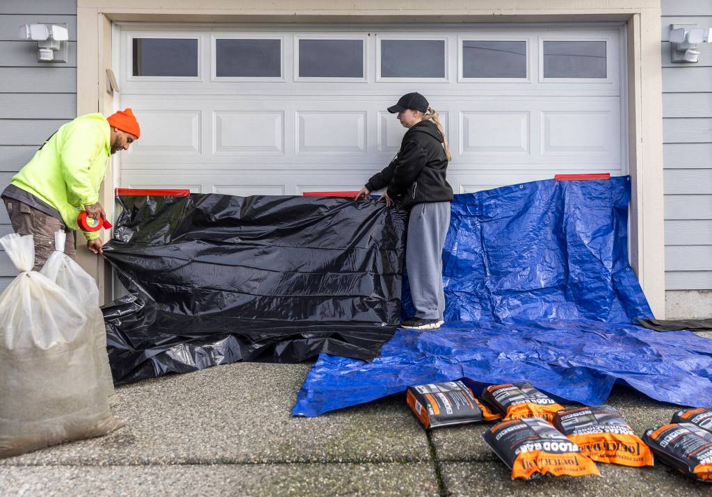 Bella Reid, right, and her fiancé Hector Rodrigues cover their garage door with tarps and water activated flood bags in preparation for potential flooding on Tuesday, Dec. 9, 2025 in Snohomish, Washington. (Olivia Vanni / The Herald)