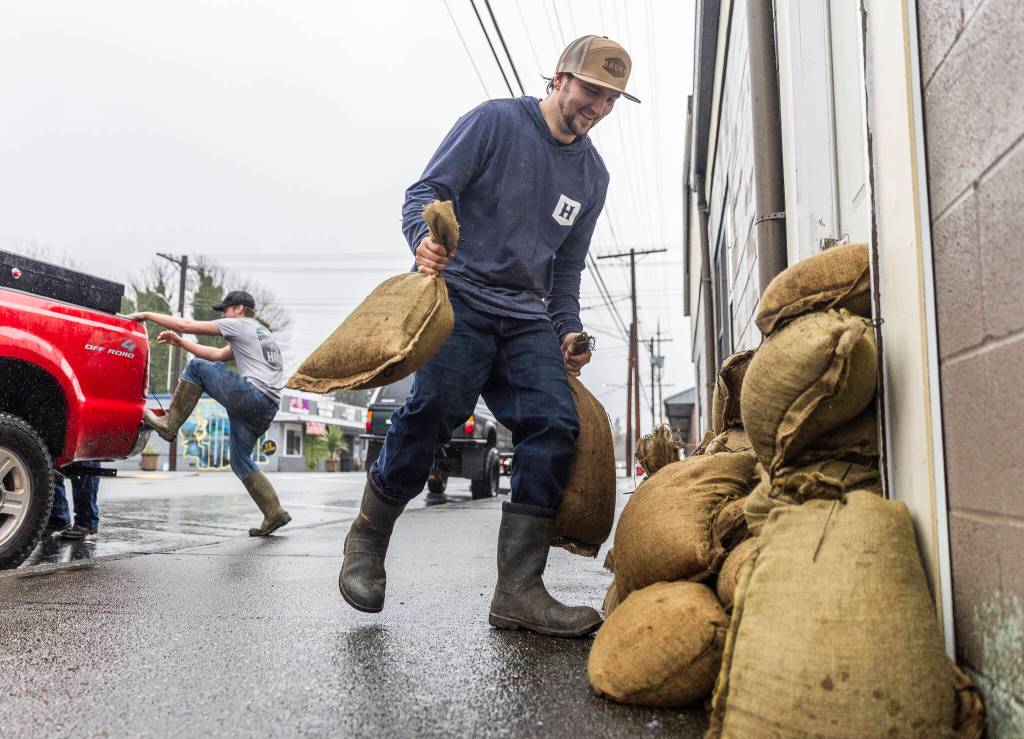Zach Day sandbags the entrance to his grandparents residence along Main Street on Wednesday, Dec. 10, 2025 in Sultan, Washington. (Olivia Vanni / The Herald)