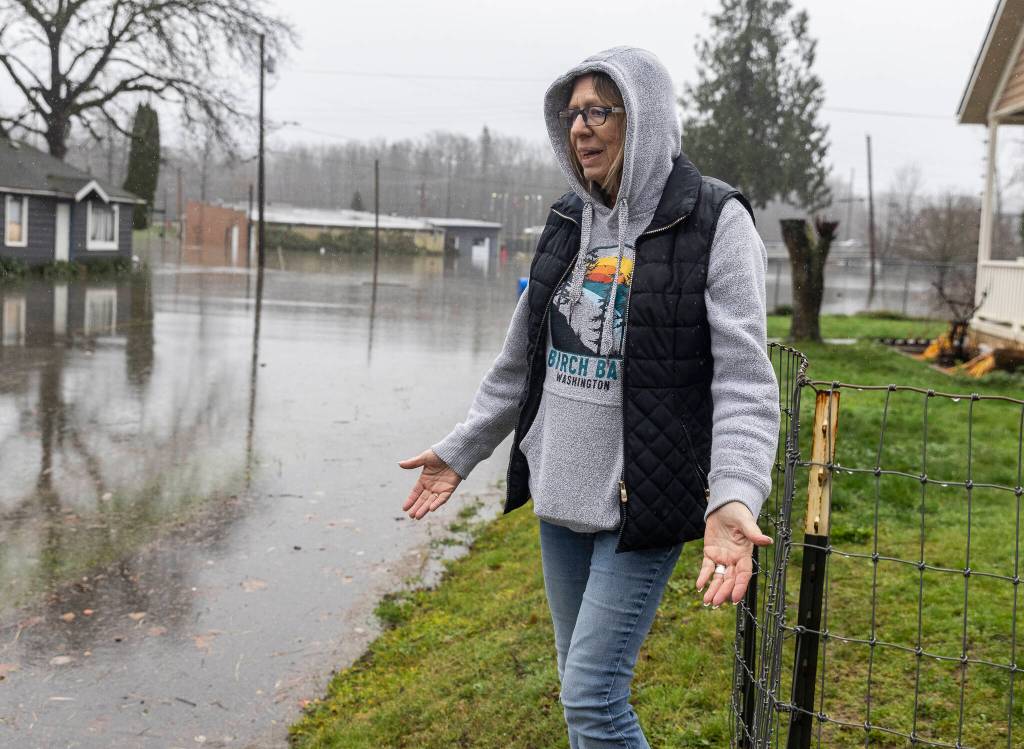 Sheryl Farmer stands in front of her home along Second Street as floodwater from the Skykomish River covers the road on Wednesday, Dec. 10, 2025 in Sultan, Washington. (Olivia Vanni / The Herald)