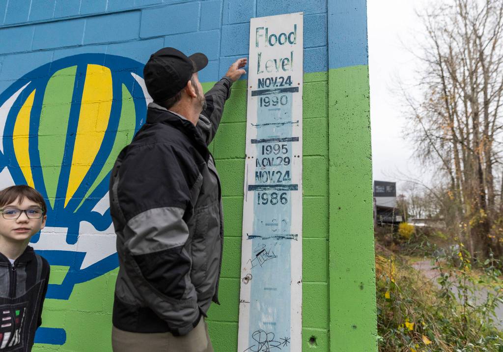 Ken Cradduck and his son Jedi, 10, look at the historic flood level markings at the base of a building along the Snohomish River Trail on Tuesday, Dec. 9, 2025 in Snohomish, Washington. (Olivia Vanni / The Herald)