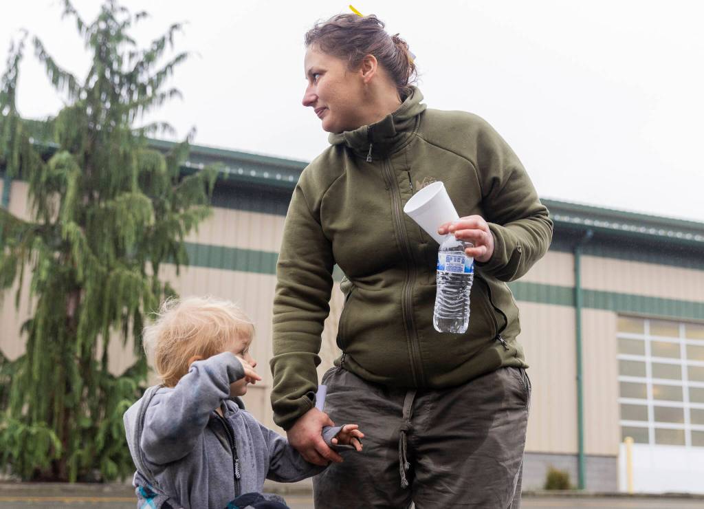 Ashlie Coffin holds the hand of her son Junior, 2, outside of the Evergreen State Fairgrounds Red Cross disaster relief shelter where her and her two sons have been staying for the last two days after their trailer at Three Rivers Mobile Home Park flooded on Friday, Dec. 12, 2025 in Monroe, Washington. (Olivia Vanni / The Herald)