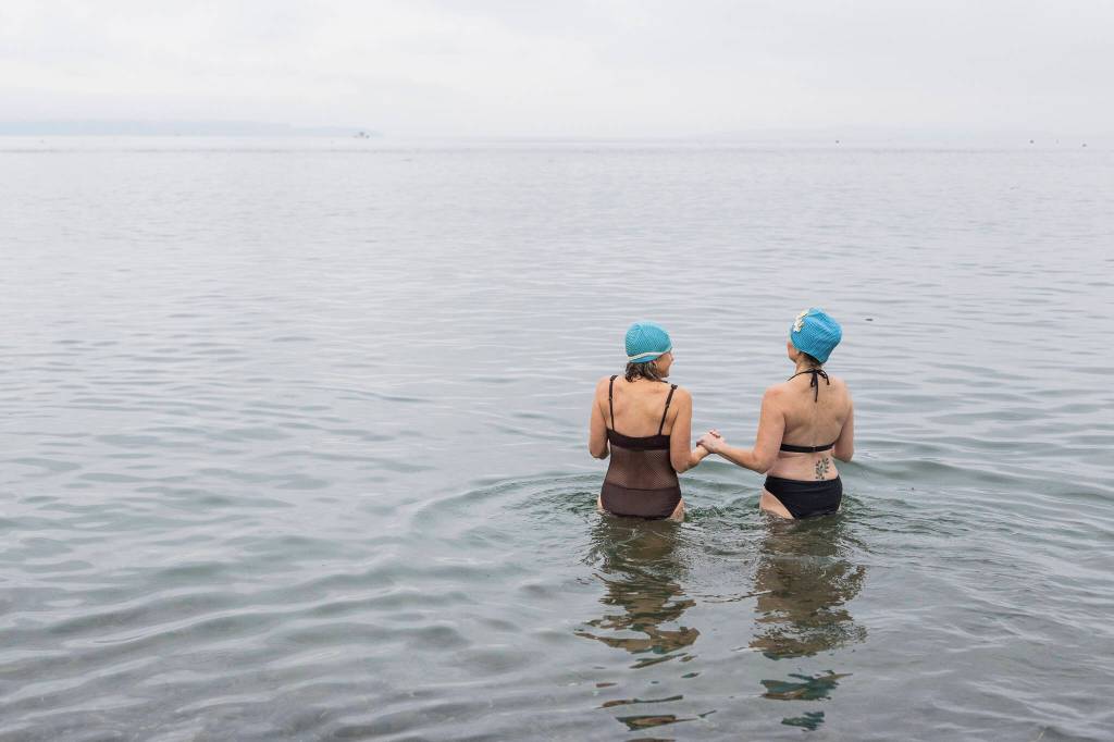 People in matching swim caps hold hands as they walk into the water at Bracketts Landing North during the 19th annual Polar Bear Plunge on Thursday, Jan. 1, 2026 in Edmonds, Washington. (Olivia Vanni / The Herald)