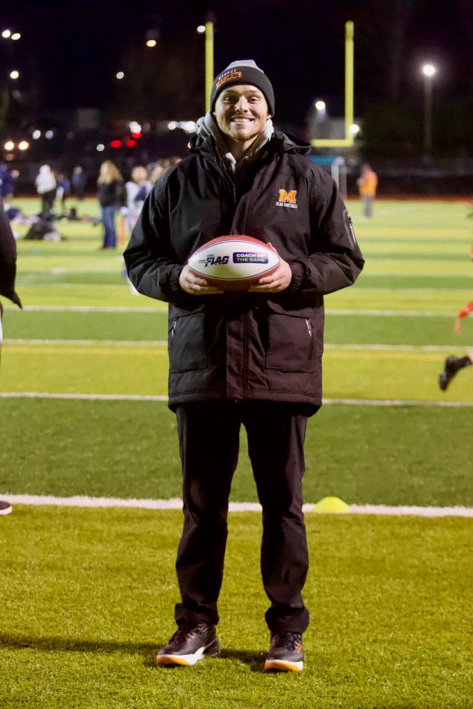 Monroe girls flag football coach Connor Wood poses with the Coach of the Game football, which he received along with a $1,000 donation to the Bearcats program after they defeated Ferndale 21-14 at the Seattle Seahawks takeover event at Everett Memorial Stadium on Jan. 7, 2026. (Joe Pohoryles / The Herald)