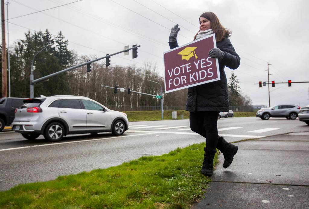 Jaime Benedict, who works as a substitute teacher, waves to drivers on the corner of Mukilteo Speedway and Harbor Pointe Boulevard while holding a sign in support of the $240 million capital bond proposal for Mukilteo School District on Tuesday, Feb. 11, 2020 in Mukilteo, Wash. (Olivia Vanni / The Herald)