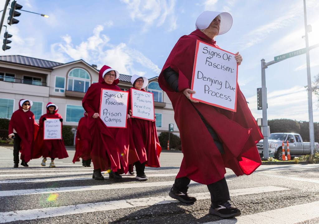 Shelly Ehni, with Edmonds United Methodist, crosses Sunset Avenue while holding a sign during South Snohomish County Indivisibles Signs of Fascism protest on Tuesday, Jan. 20, 2026 in Edmonds, Washington. (Olivia Vanni / The Herald)