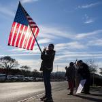 Valerie Heer holds an American flag and flashes a peace sign with her hand to cars driving along Sunset Avenue during South Snohomish County Indivisibles Signs of Fascism protest on Tuesday, Jan. 20, 2026 in Edmonds, Washington. (Olivia Vanni / The Herald)