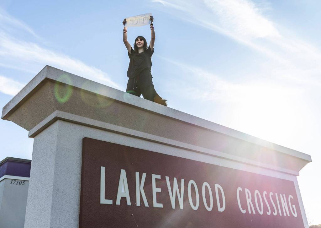Anayah Ulrich holds a sign while standing on top of the Lakewood Crossing entrance sign during a student walkout and protest on Thursday, Feb. 5, 2026 in Marysville, Washington. (Olivia Vanni / The Herald)