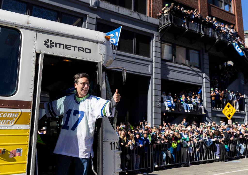 Washington Gov. Bob Ferguson waves at fans from a bus along 4th Avenue during the Seahawks World Champions Parade on Wednesday, Feb. 11, 2026, in Seattle, Washington. (Olivia Vanni / The Herald)