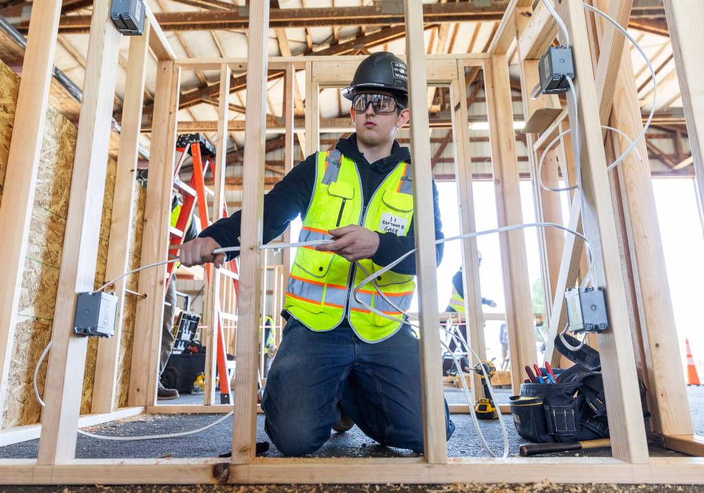 Gage Wolfe, a senior at Arlington High School, threads wire through wall studs on Tuesday, Feb. 10, 2026 in Marysville, Washington. (Olivia Vanni / The Herald)