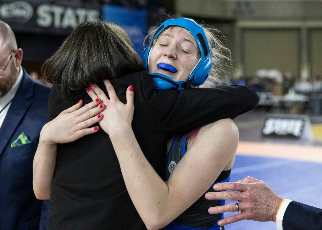 Shorewoods Finley Houck hugs one of her coaches after winning the 3A girls 115-pound championship match at the Mat Classic on Friday, Feb. 20, 2026 in Tacoma, Washington. (Olivia Vanni / The Herald)