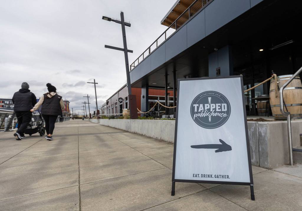 People walk along the water past the entrance to the new Tapped Public House at the Port of Everett on Tuesday in Everett.