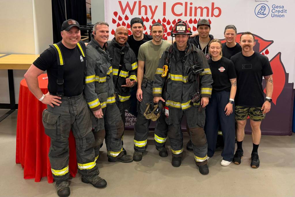 Members of the Everett Fire Department gather around battalion chief D.J. Neyens (red helmet), who is undergoing chemotherapy for multiple myeloma, as he prepares to climb the stairs to the 73rd floor of the Columbia Tower at the Blood Cancer Uniteds Firefighter Stairclimb on Sunday in Seattle. (Aaron Coe / The Herald)