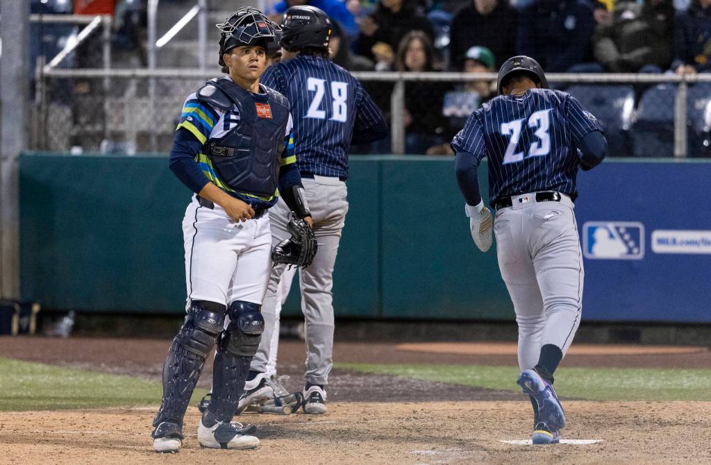 Luke Stevenson (32) of the Everett AquaSox looks on as Anthony Scull (23) of the Tri-City Dust Devils scores the 15th run during the fourth inning on Tuesday, April 7, 2026 in Everett, Washington. (Olivia Vanni / The Herald)