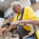 John Ellis sands the side of a dulcimers frame in preparation for a small repair in his workshop on Thursday, May 7, 2026 in Arlington, Washington. (Olivia Vanni / The Herald)