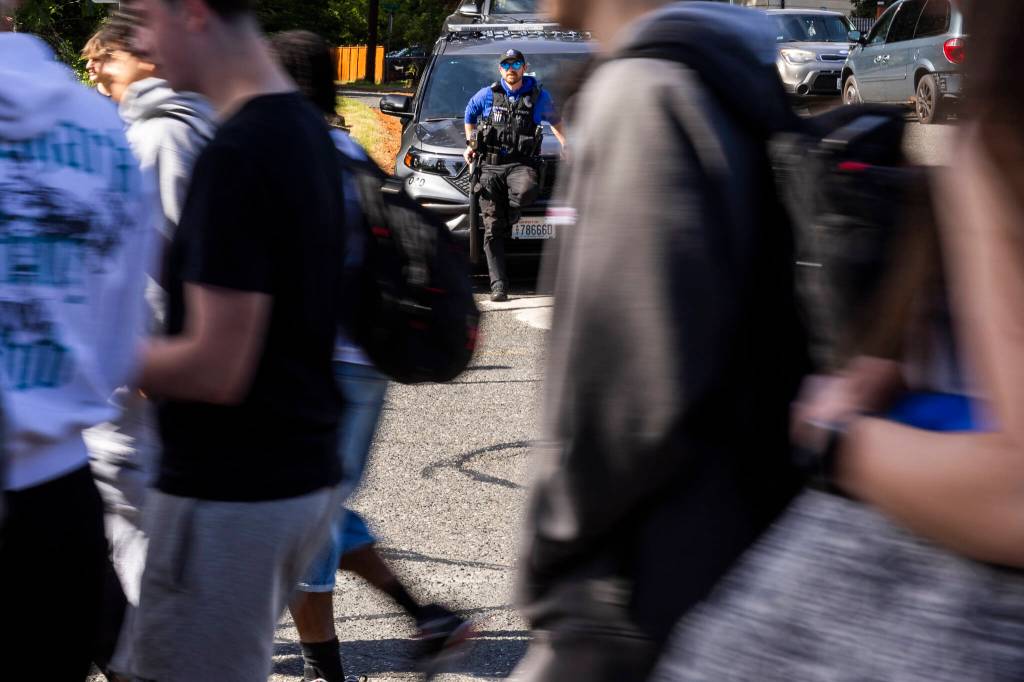 Bothell High Schools school resource officer Garrett Ware watches as students walk out of the high school in protest of the school boards vote to not renew the contract for his position at the school on Monday, May 18, 2026, in Bothell, Washington. (Olivia Vanni / The Herald)