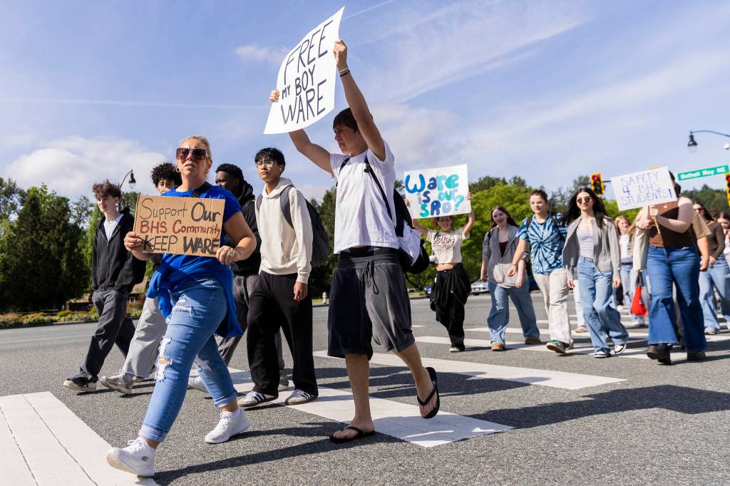 Jelena Krzeszowski and her son, Stefan Krzeszowski, hold signs in protest of the school boards vote to not renew the contract for Bothell High Schools school resource officer on Monday, May 18, 2026 in Bothell, Washington. (Olivia Vanni / The Herald)