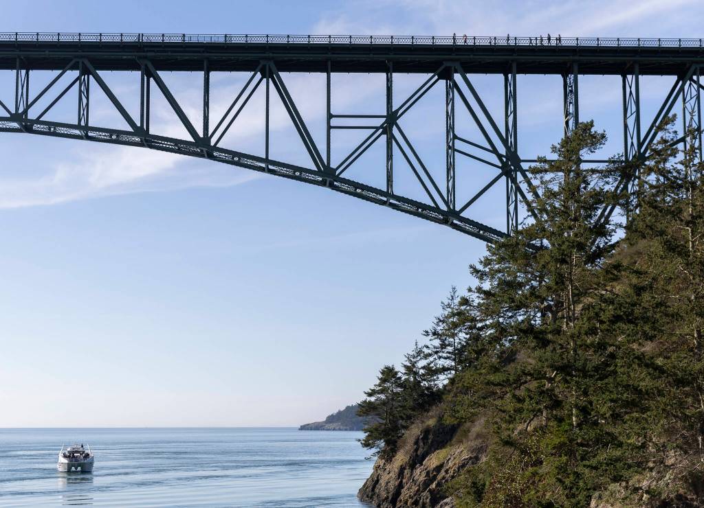 People walk across Deception Pass Bridge as a whale watcher boat passes underneath on Monday, March 2, 2026 in Anacortes, Washington. (Olivia Vanni / The Herald)