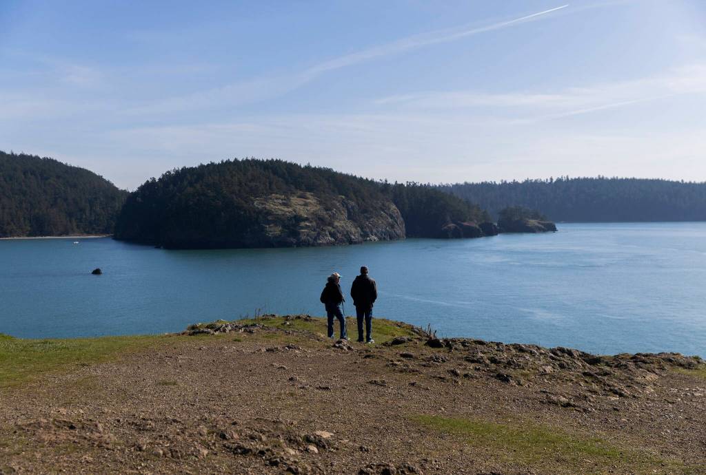 People stand at the edge of Rosario Head at Deception Pass State Park and look out toward Northwest Pass on Monday, March 2, 2026 in Anacortes, Washington. (Olivia Vanni / The Herald)