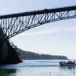 People walk across Deception Pass Bridge as a whale watcher boat passes underneath on Monday, March 2, 2026 in Anacortes, Washington. (Olivia Vanni / The Herald)
