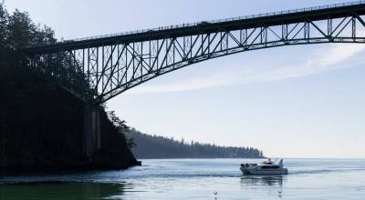 People walk across Deception Pass Bridge as a whale watcher boat passes underneath on Monday, March 2, 2026 in Anacortes, Washington. (Olivia Vanni / The Herald)