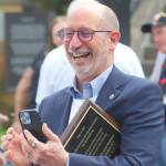 Edmonds Mayor Mike Rosen takes a photo while holding a plaque honoring Edmonds as the nations first community of service during a launch for Edmonds Serves on Saturday, June 6, 2026, in Edmonds, Washington. (Michael Henneke / The Herald)